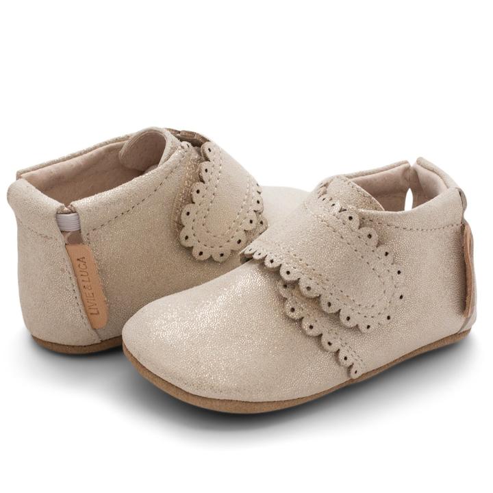 A darling and easily matchable boot for baby, Fleur offers a single hook-and-loop closure that make for easy on and off. Stage: crawling Suede shimmer upper Natural leather lining Adjustable hook and loop closure for a tailored fit Padded elastic collar for easy on and off Tan suede sole with black recycled rubber tread circles Best suited for indoor use and light outdoor activity APMA approved sole